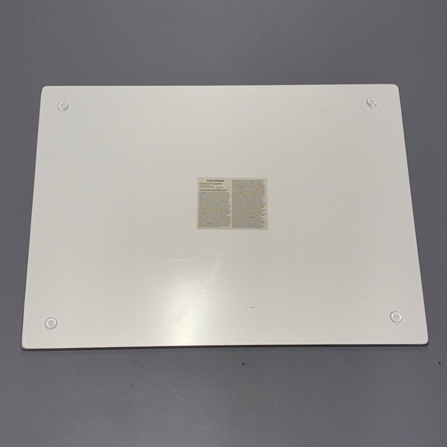 A white rectangular metal panel with rounded corners, four screw holes, and a small instruction label in the center, photographed on a gray background.
