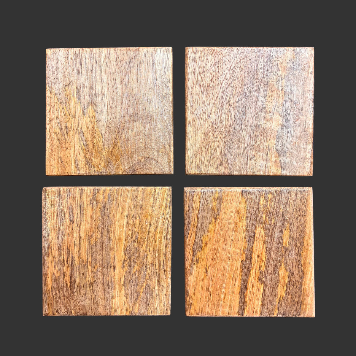 Four square Mango wood Coasters arranged in a 2x2 grid on a dark gray background, showing different natural wood tones and textures.