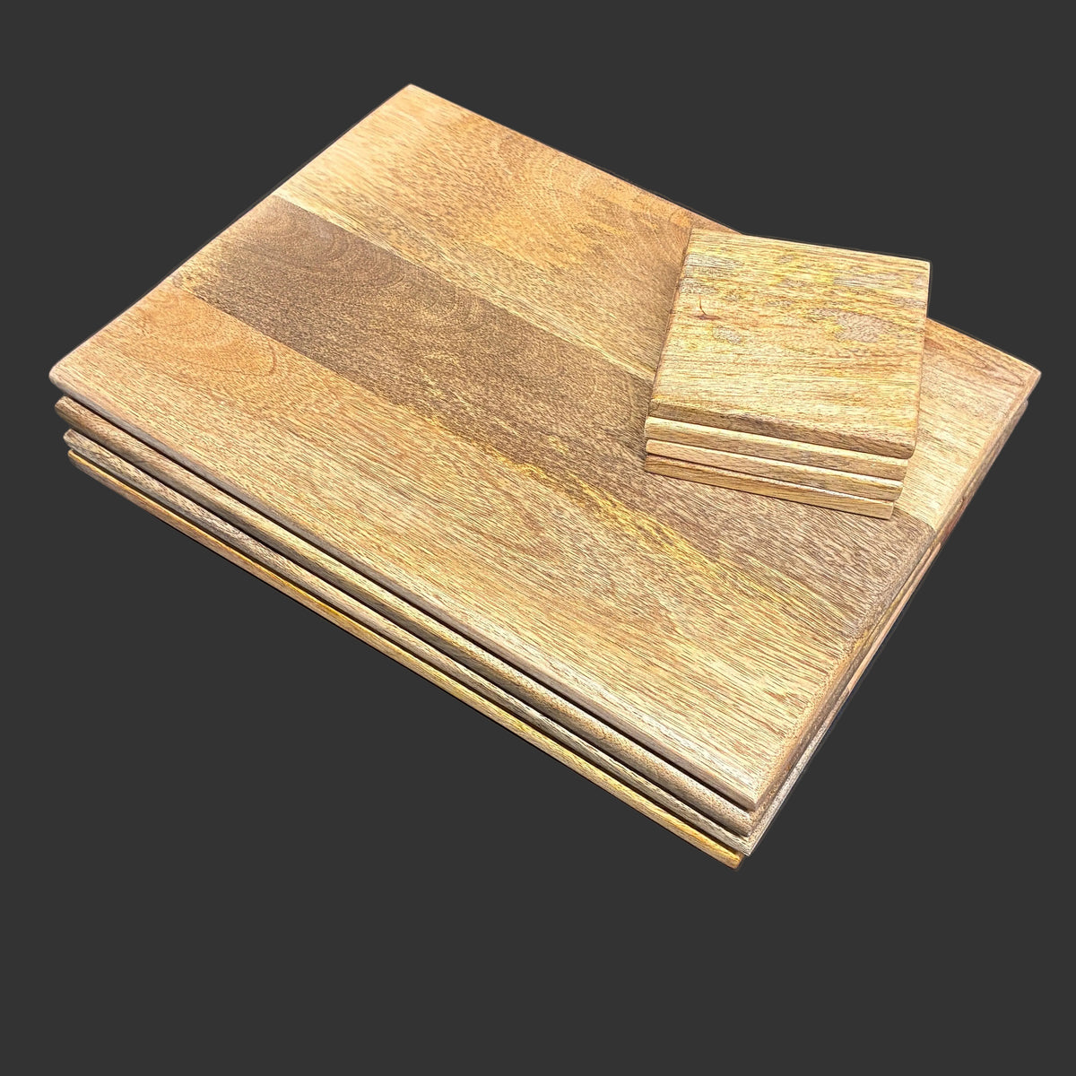 A stack of rectangular wooden boards with visible wood grain, photographed on a dark tabletop. A smaller matching stack of square wooden coasters or tiles rests on top of the larger boards.