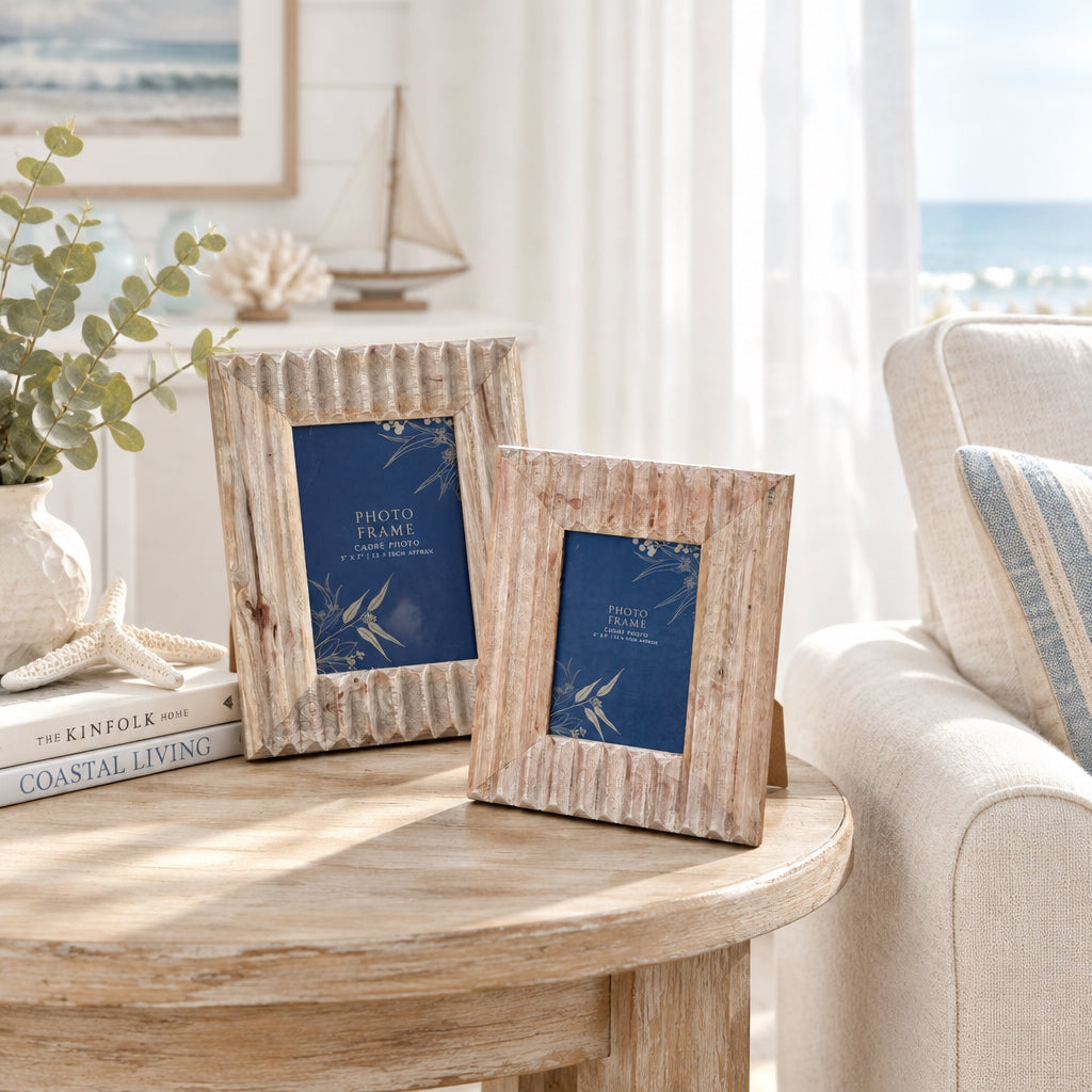 Two rustic rectangular wooden picture frames with scalloped edges, standing on asphalt pavement. The frames are natural light brown wood, and the glass inserts display a blue floral design.