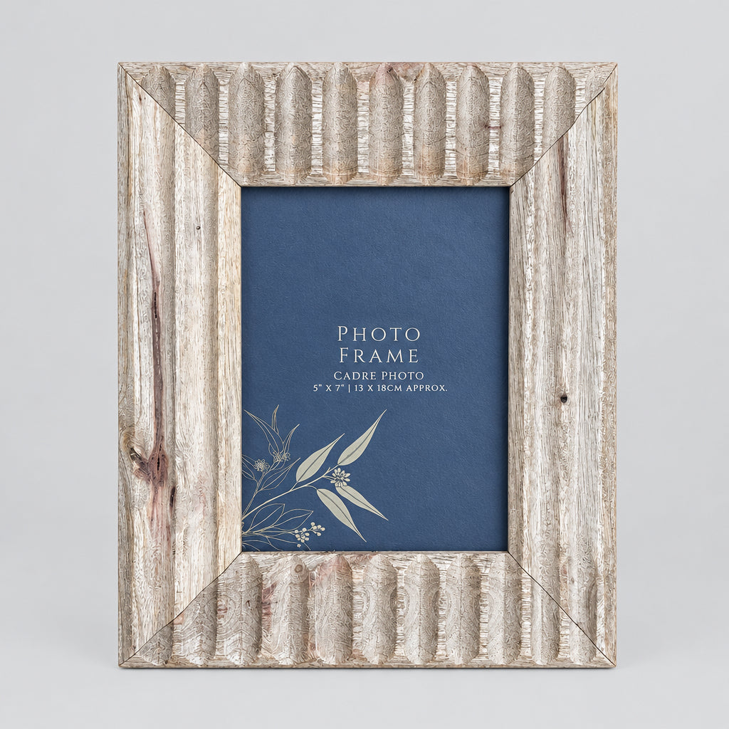 A rectangular rustic wooden picture frame with a weathered gray-brown finish and carved vertical details, holding a blue photo insert, set against a wooden plank background.