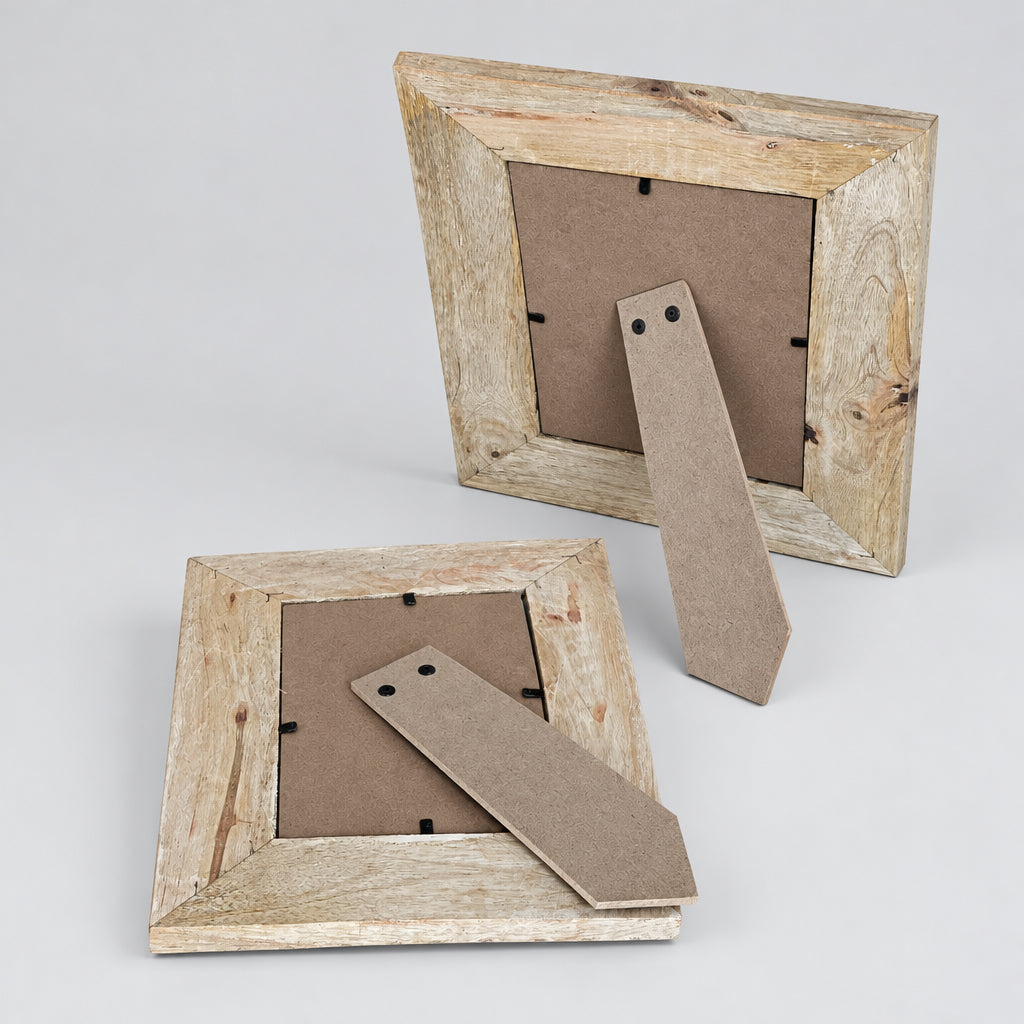 Two rustic wooden picture frames shown from the back on a wood chip surface, with cardboard hangers visible and no photos inserted.