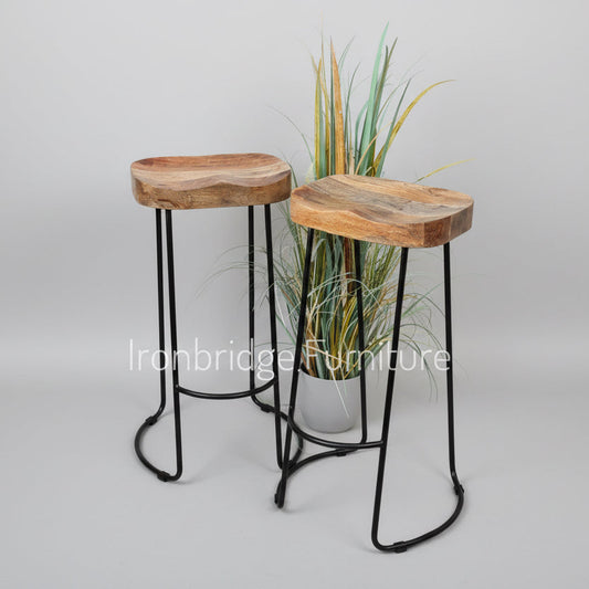 Two wooden stools with black metal legs in front of a plant on a wooden floor.