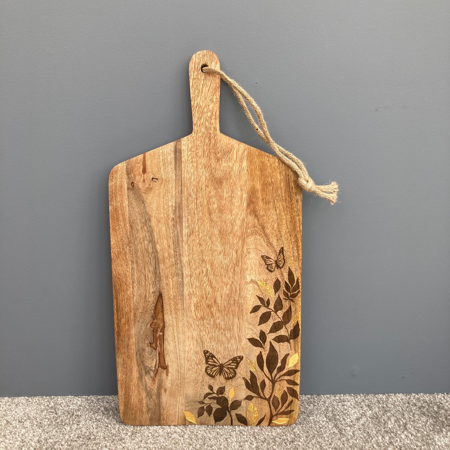 Floral design etched Mango wood food serving paddle board stood up on grey background