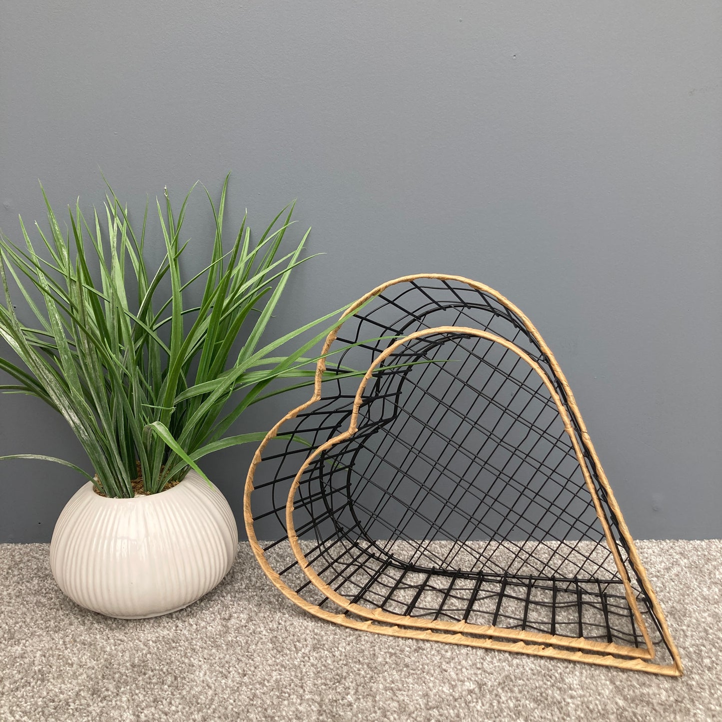 Heart shaped woven metal fruit baskets with raffia edging placed inside each other. 