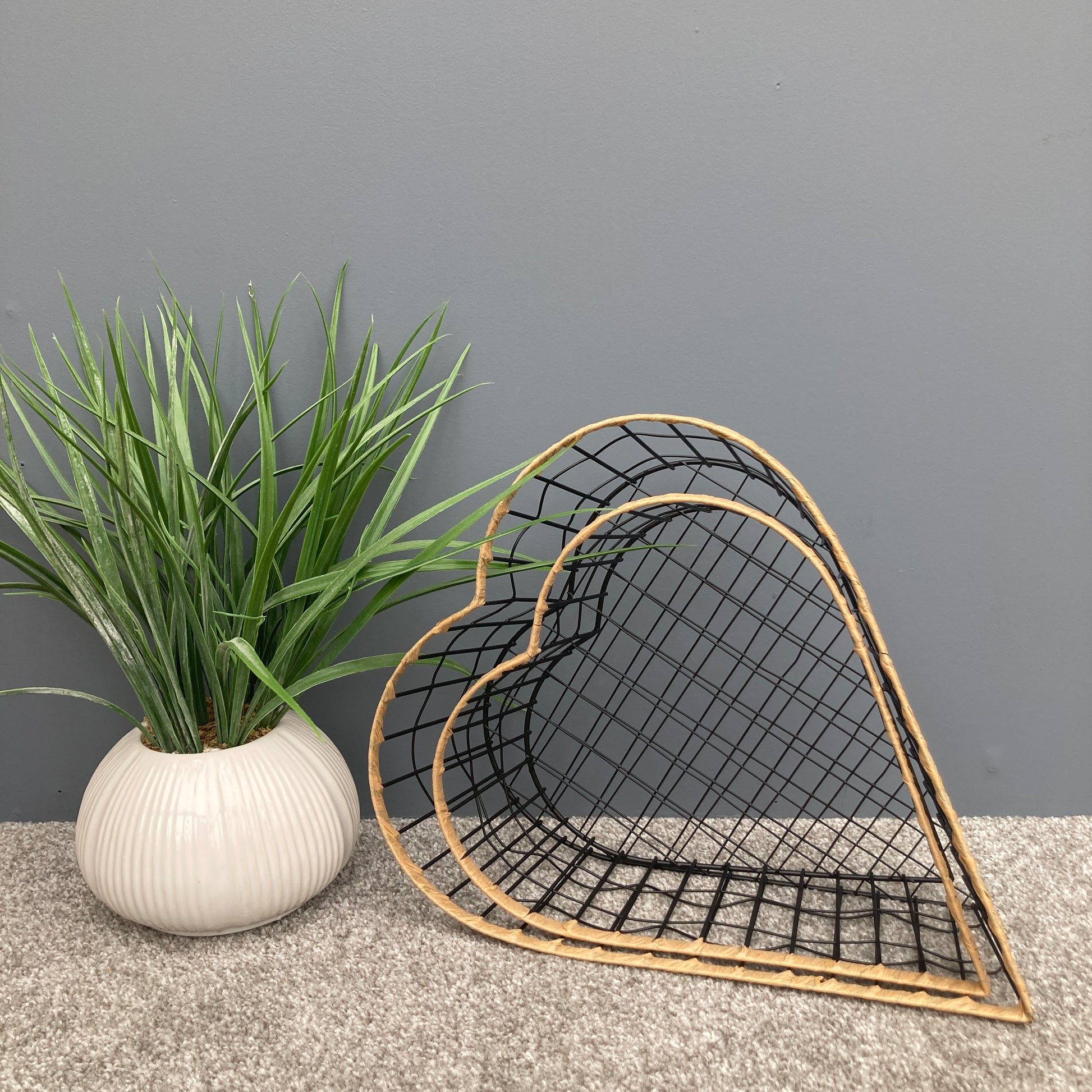Heart shaped woven metal fruit baskets with raffia edging placed inside each other. 