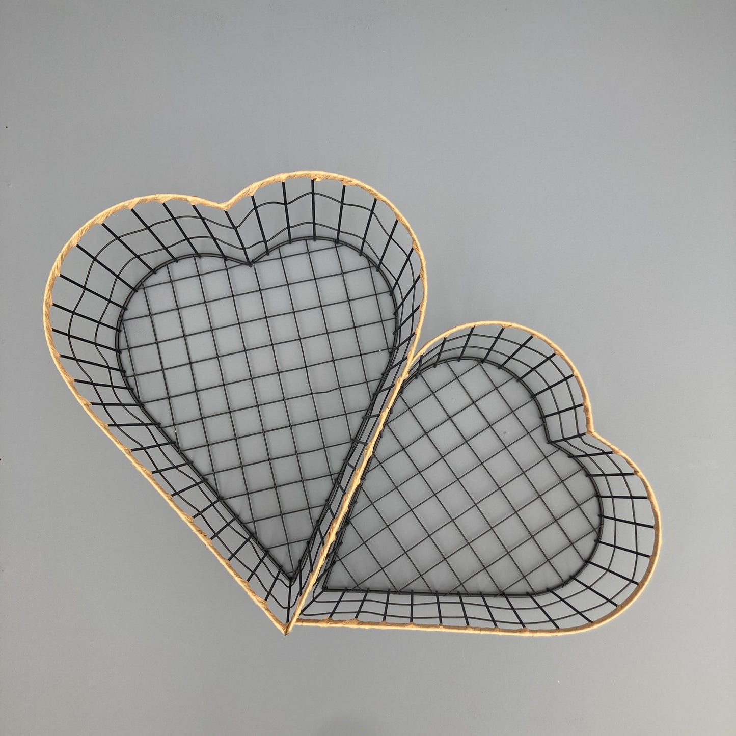 Heart shaped woven metal fruit baskets with raffia edging placed side by side.