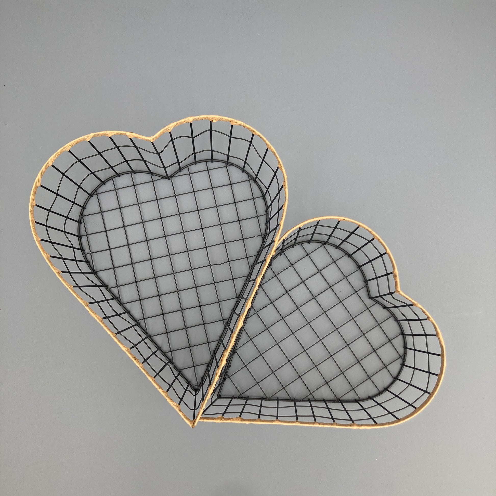 Heart shaped woven metal fruit baskets with raffia edging placed side by side.