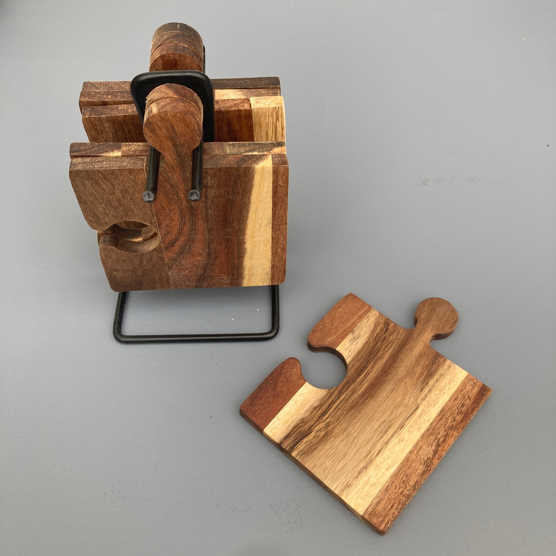 Set of 6 Acacia wood puzzle shaped coasters on a metal holder. View of coaster and holder.