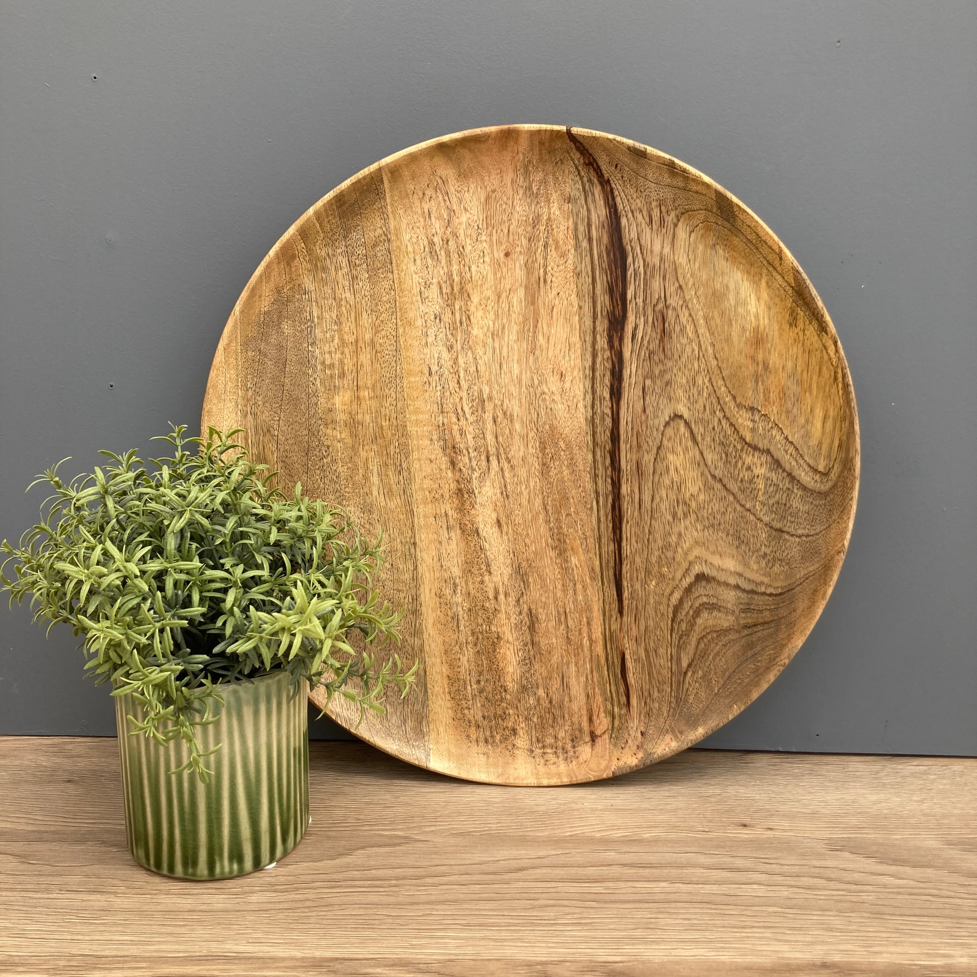 Solid Mango plate on a counter with a green pot and vase