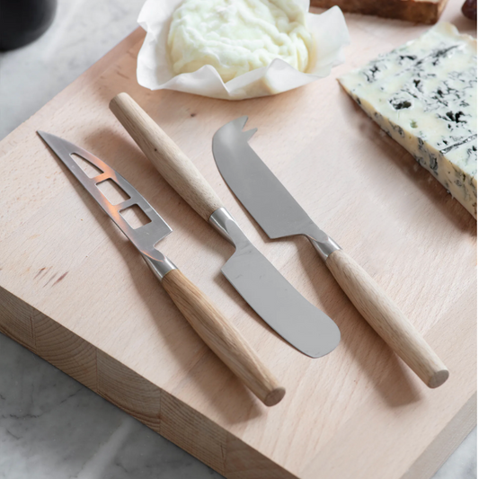 Set of cheese knives on a wooden cutting board with cheese and butter on a marble surface
