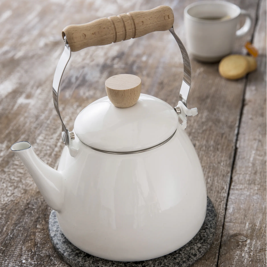 White kettle with wooden handle and lid knob on a wooden surface