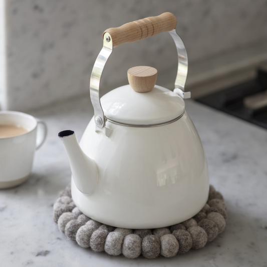 White kettle with wooden handle and lid knob on a marble surface with a cup of tea.