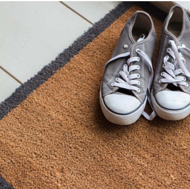 Pair of gray sneakers with white soles on a brown doormat.