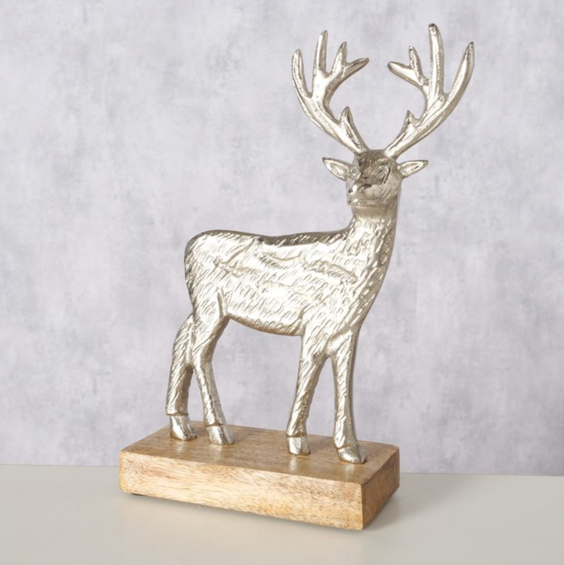Decorative silver deer figure on a wooden base against a light gray background