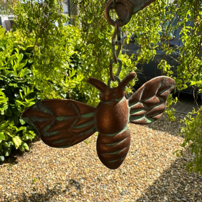 Decorative metal moth hanging from a chain against a green outdoor background