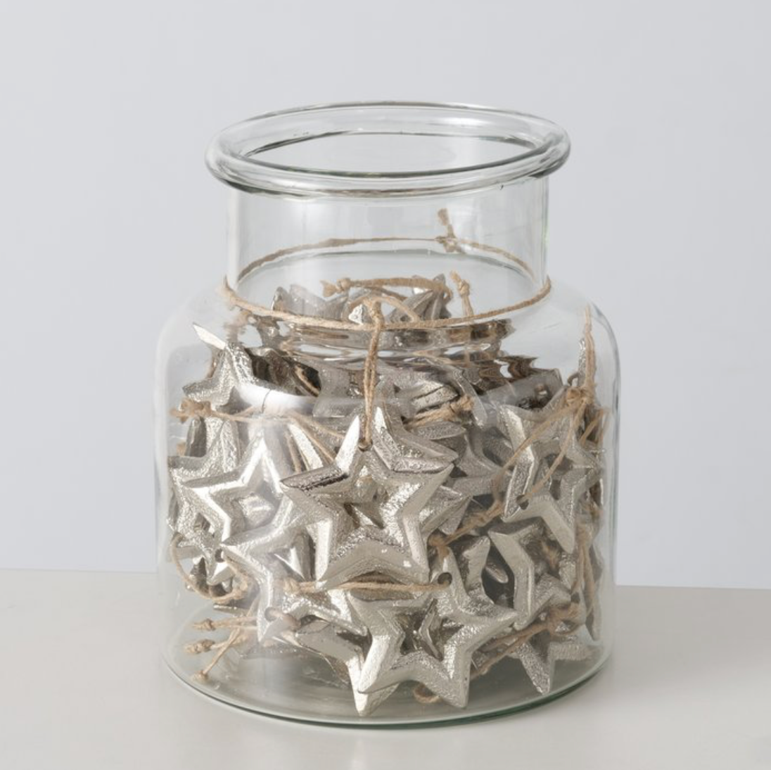 Clear glass jar filled with silver star-shaped objects on a white background