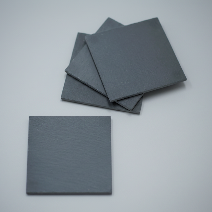 Four dark gray square slate coasters on a wooden surface