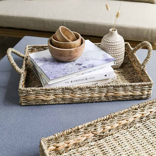Woven tray with books, bowls, and a vase on a coffee table.