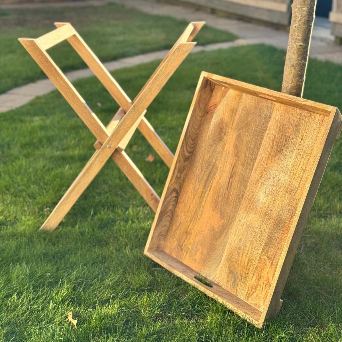 Sloping edge butler tray on foldable stand - Mango wood. tray leaning against tree.