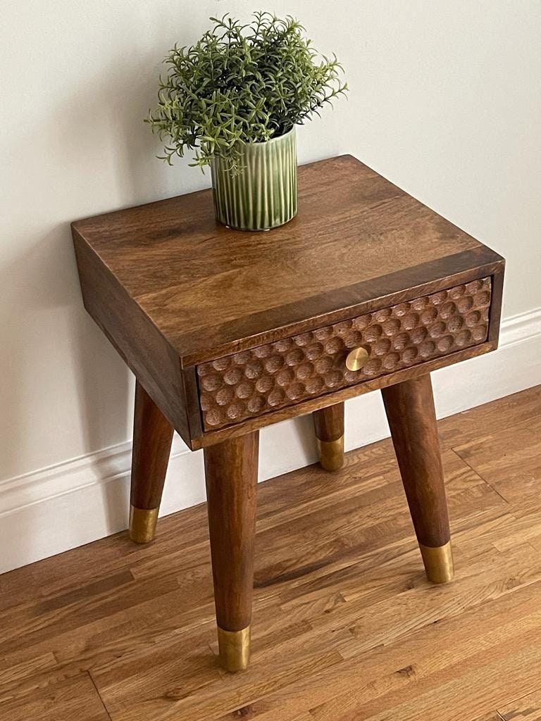 Dark Mango wood side table with 1 carved drawer and tapered legs with potted plant on top. 