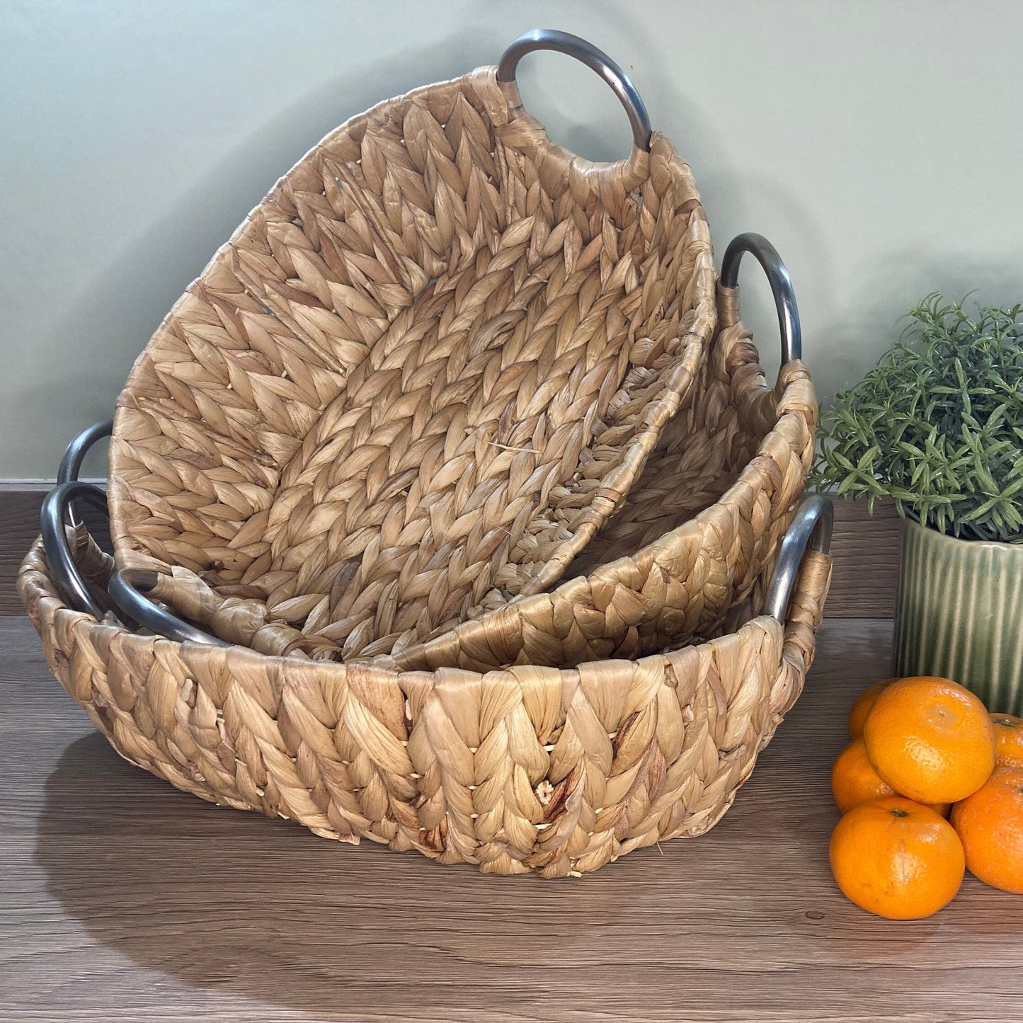 Woven water hyacinth fruit baskets with aluminium loop handles. Shown with oranges.